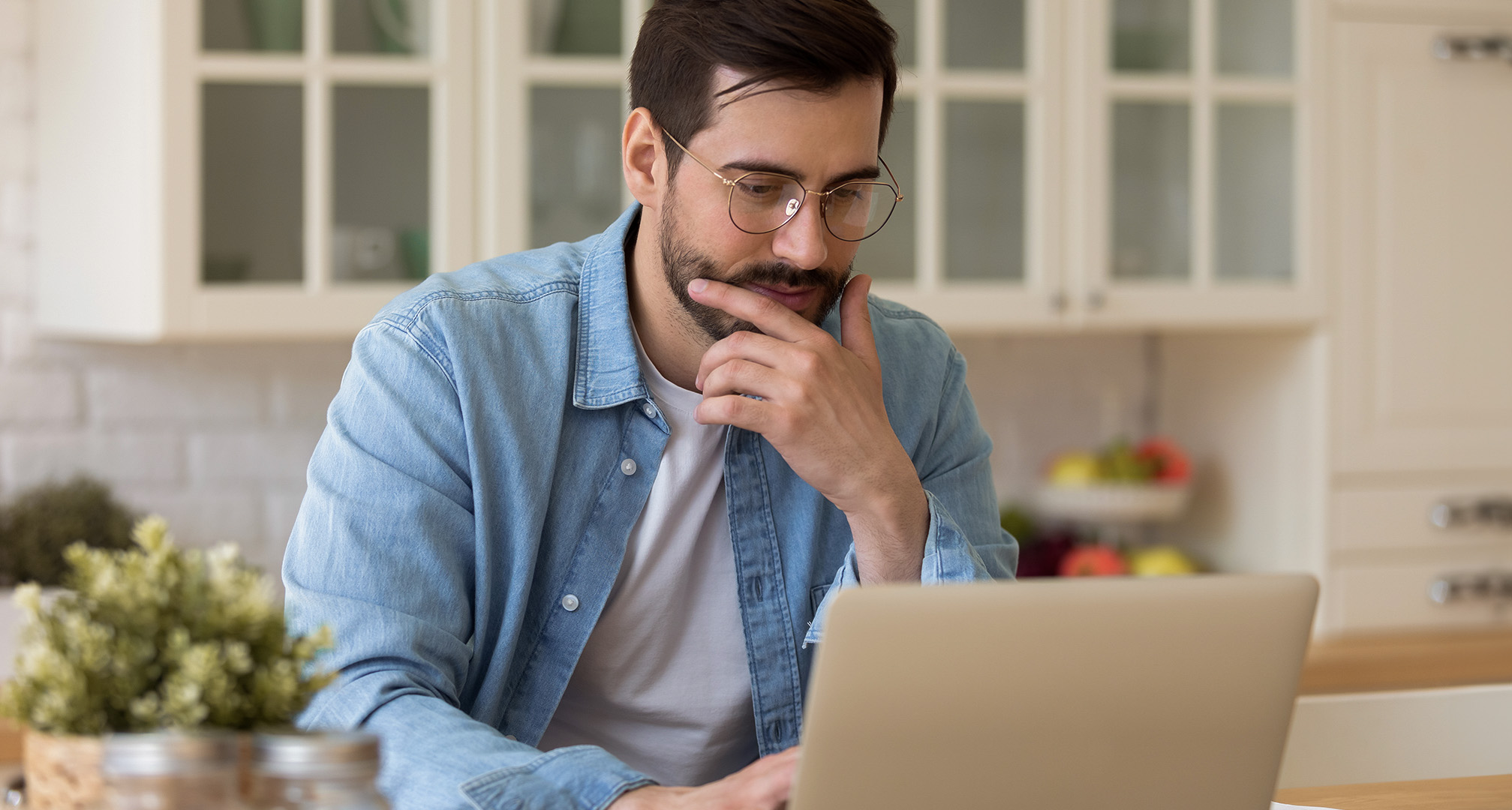 personne avec des lunettes assise dans une cuisine et regardant un ordinateur portable