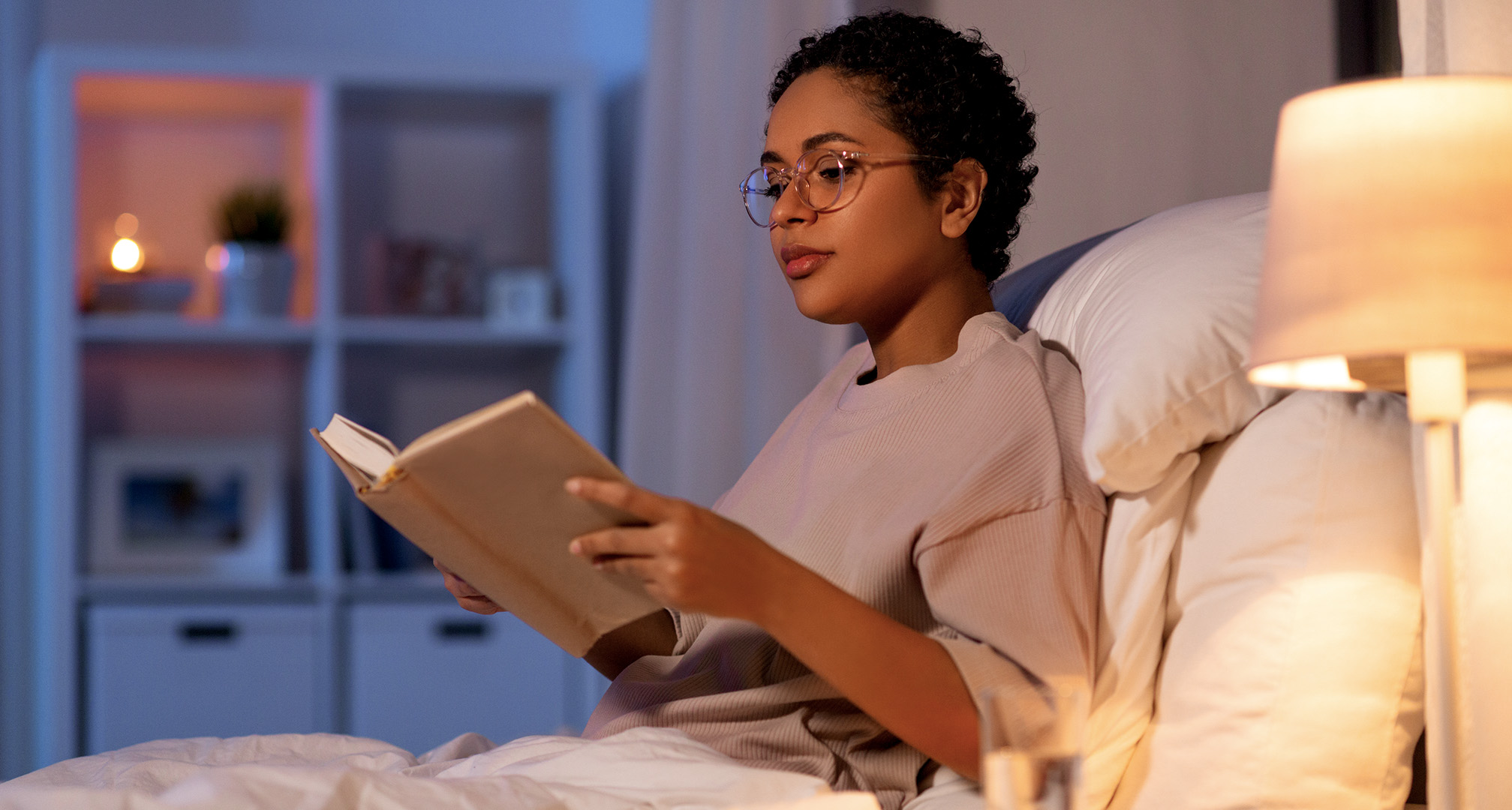 personne portant des lunettes et lisant un livre dans une pièce faiblement éclairée